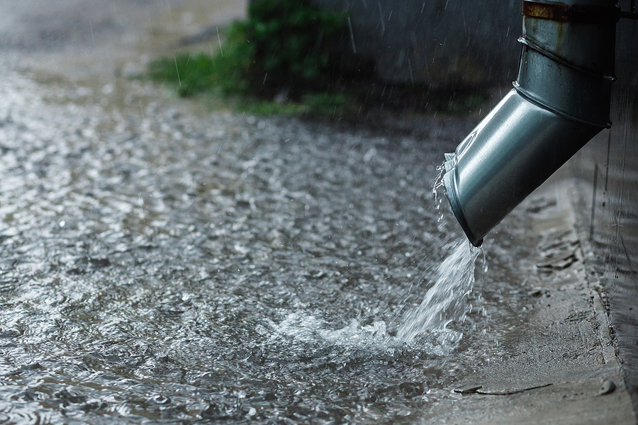 A downspout spewing water into a flooded yard, depicting why you should have a graded slope.