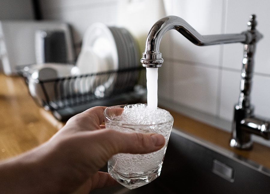 A man filling a glass with water from a kitchen sink faucet to stress the importance of inspecting water pressure and flow