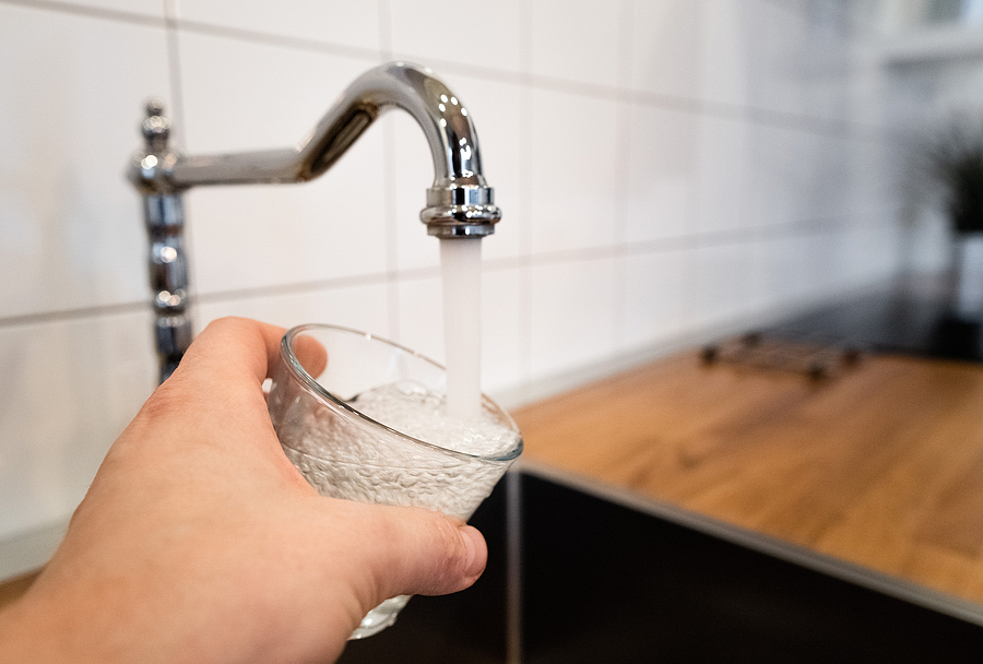 A hand holding a glass under a faucet that is running at a high water pressure.