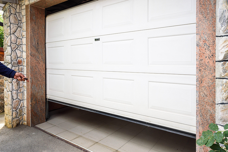 A white garage door on an attached garage being opened with a remote garage door opener.