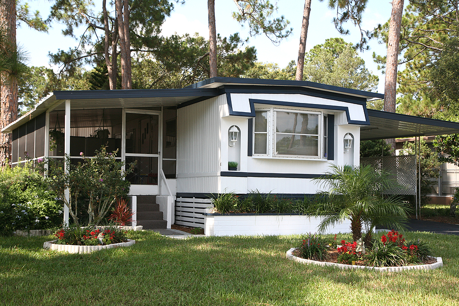 A white single wide mobile home with a blue roof and a green yard.