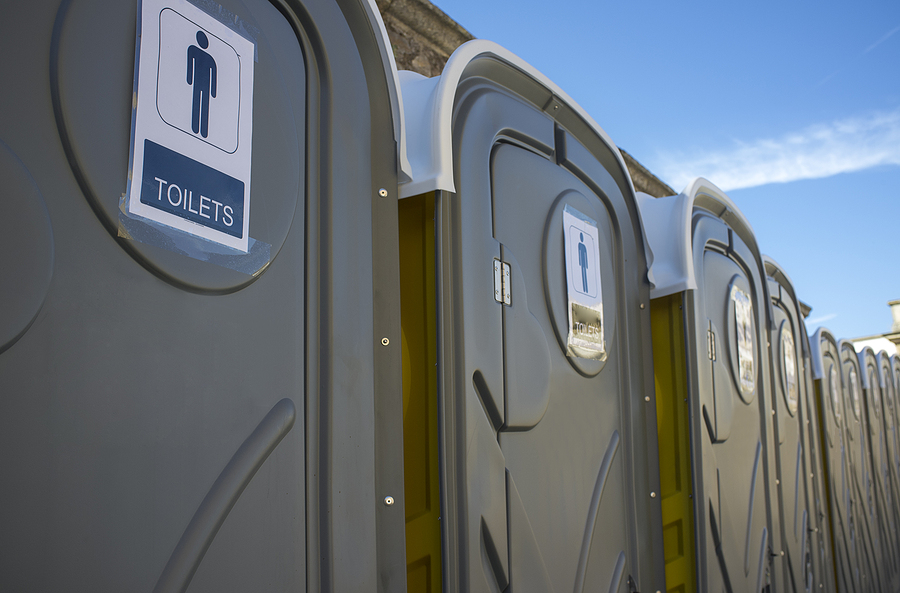A close up of gray, rented portable toilets under a blue sky. 